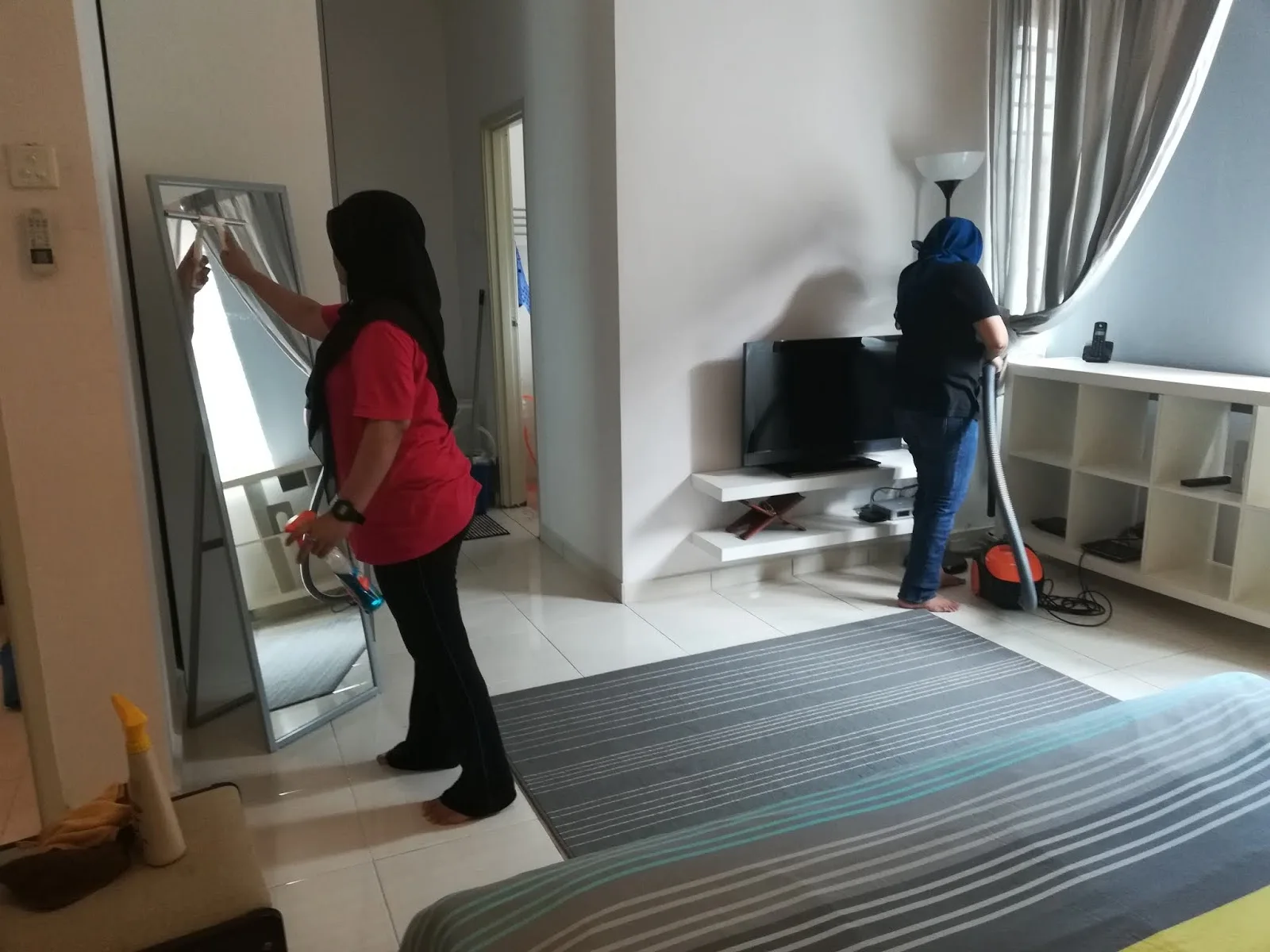 Dua tukang cuci mengelap cermin dan menyedut lantai bilik semasa pembersihan rumah